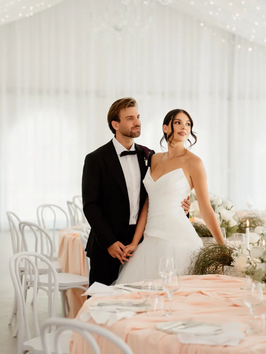 Groom in a black tuxedo with his bride at a wedding reception